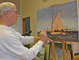 An older man painting a sailboat.