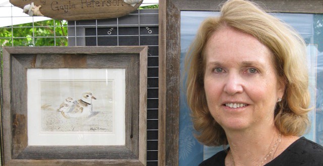 A woman standing next to a framed piece of art.