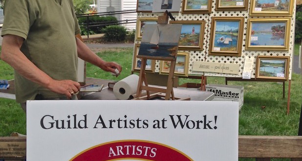A man standing in front of a sign that says guild artists at work art show.