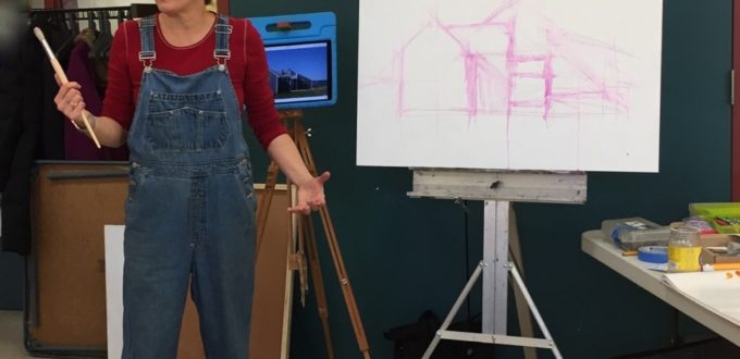 A woman in overalls standing in front of an easel.