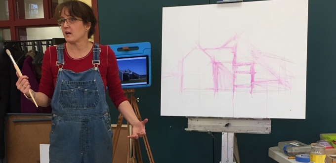 A woman in overalls standing in front of a easel.