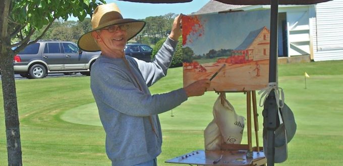 A man in a hat painting on an easel.