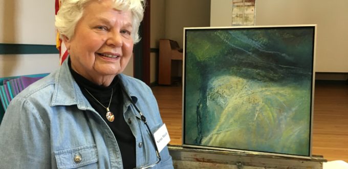 An older woman standing in front of a painting.