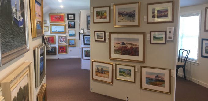 A room full of framed paintings in a gallery.