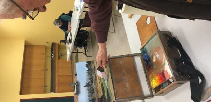 An older man looking at a painting on a table.