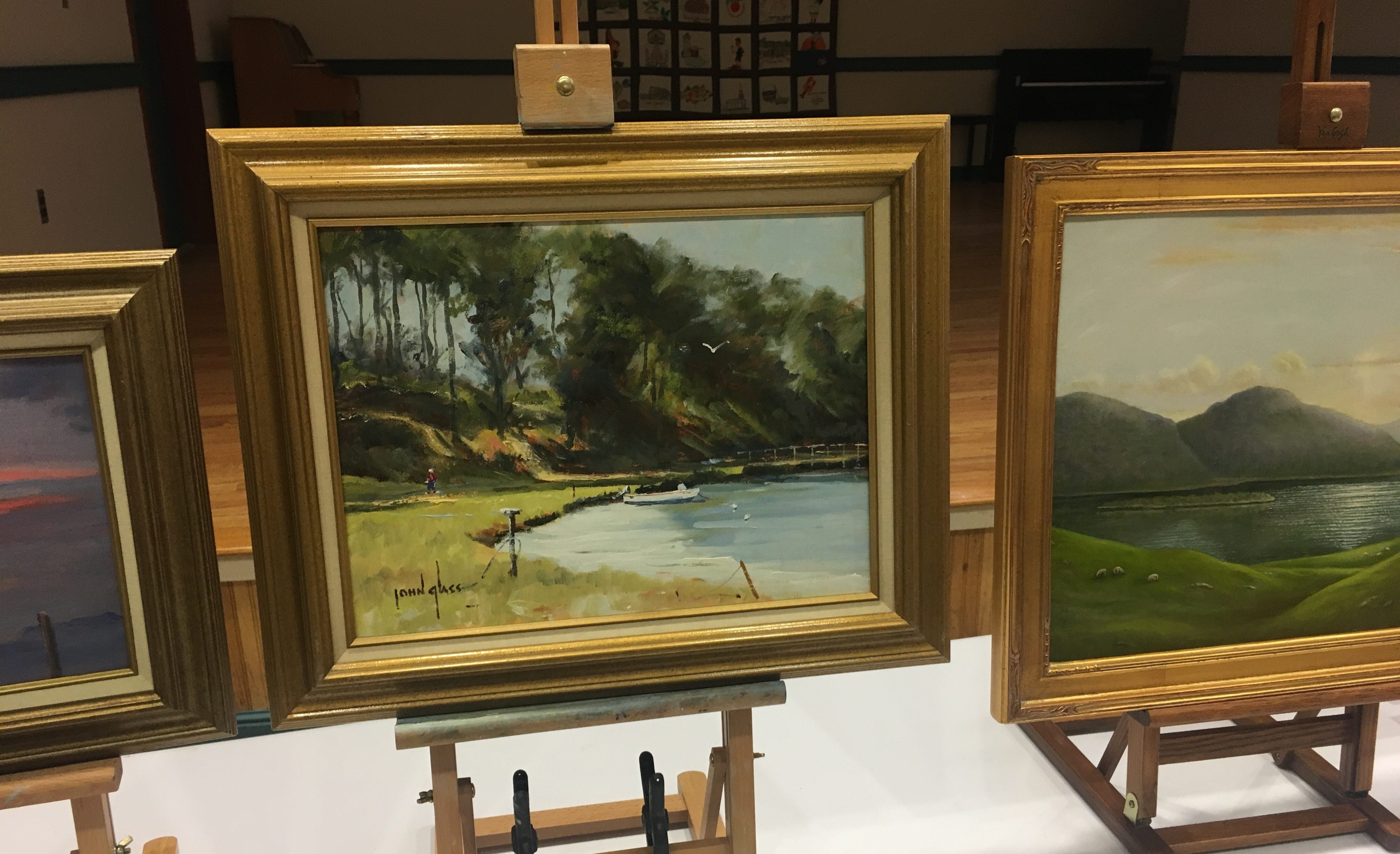 Three framed paintings on easels in front of a table.