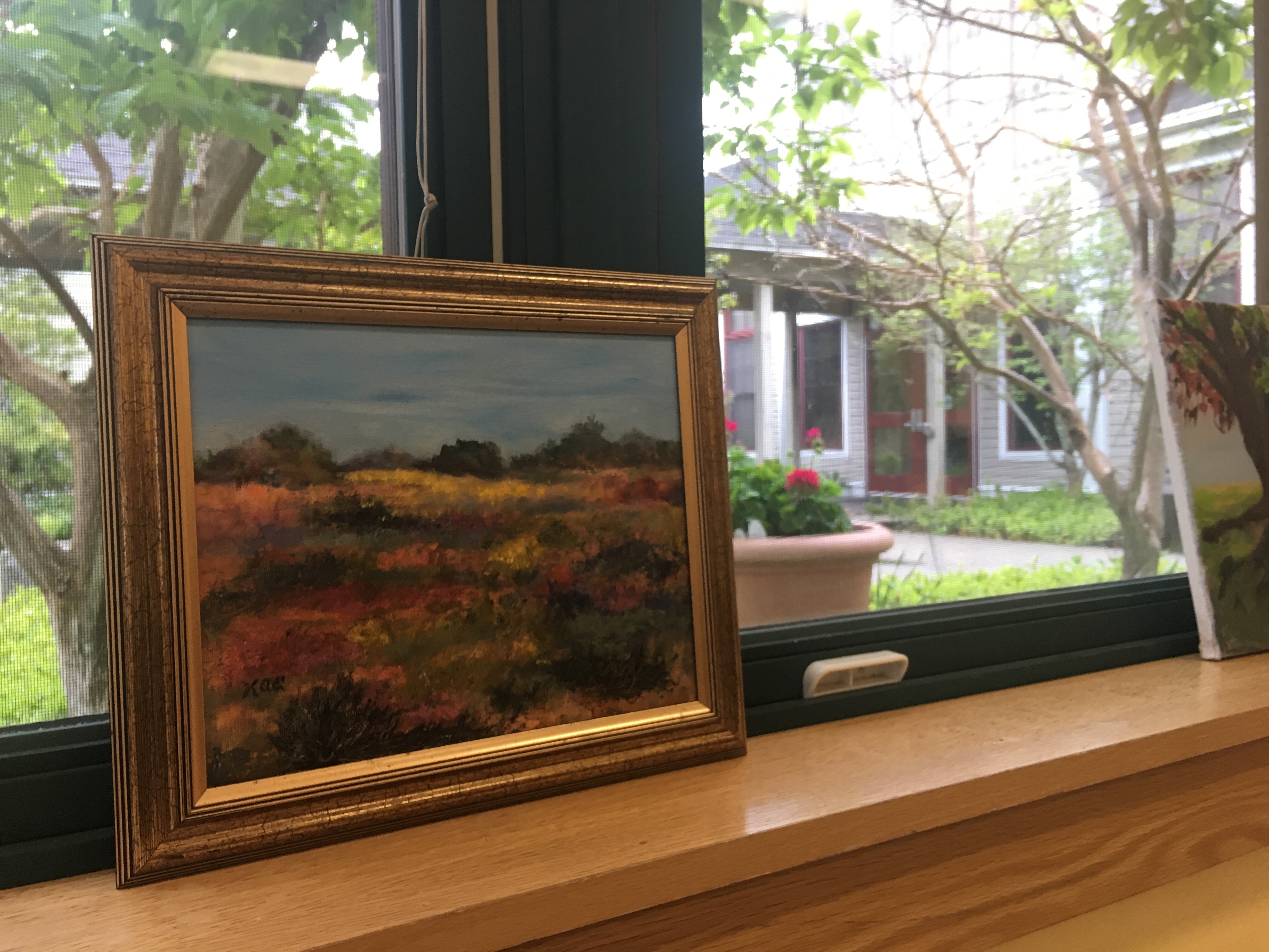 A framed painting sits on a window sill.