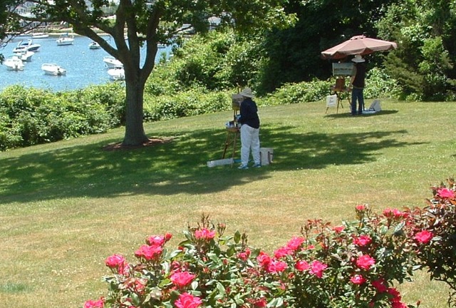 A man is painting on a lawn near a body of water.