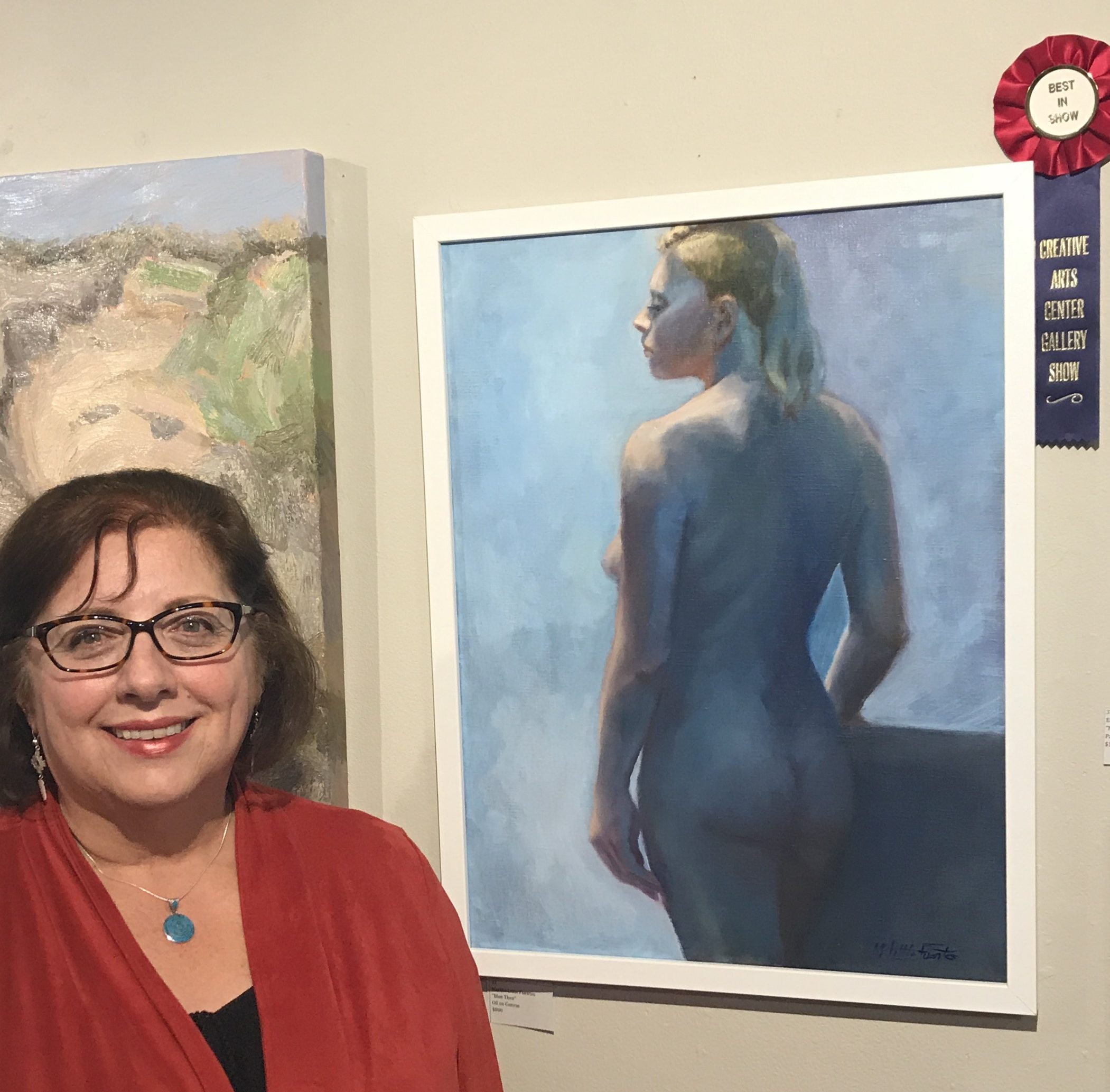 A woman standing in front of a painting of a nude woman.