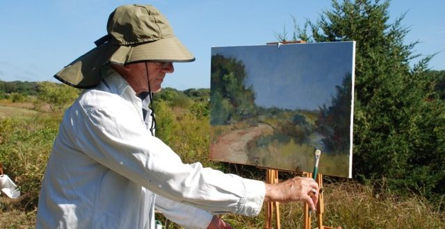 A man in a hat is painting in the field.