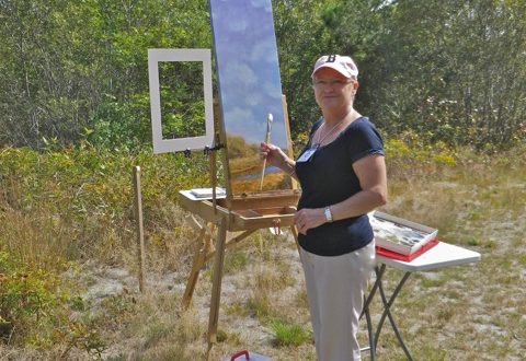 A woman standing next to an easel in a field.