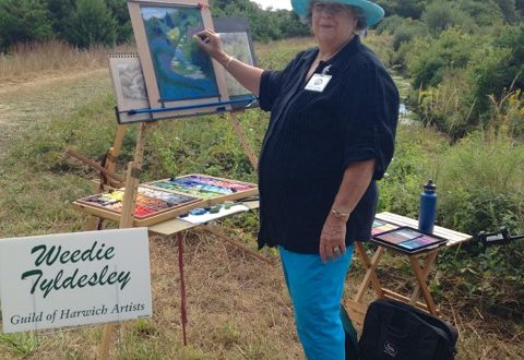 A woman in a blue hat standing next to an easel.