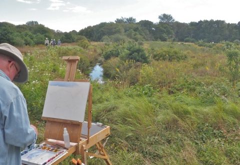 A man is painting in a field with an easel.
