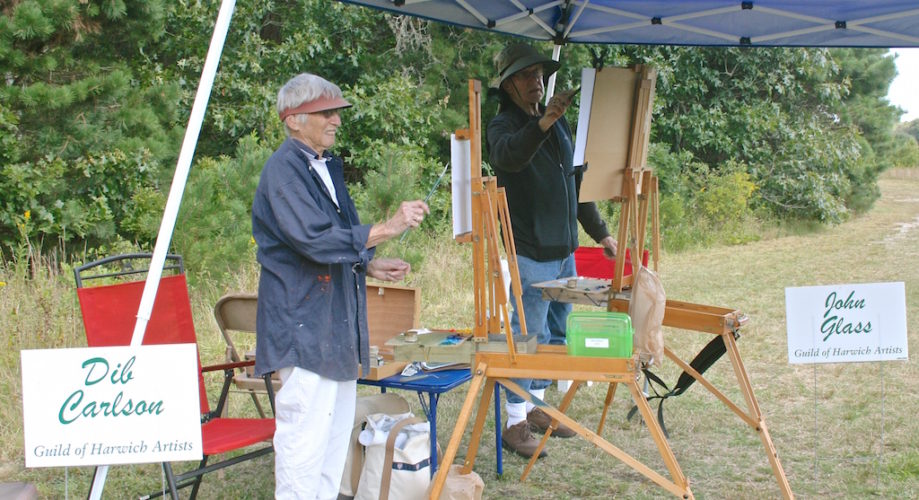 A man with a easel in front of a tent.