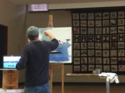 A man painting on an easel in a classroom.