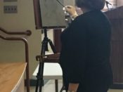 A woman is painting on an easel in a room.