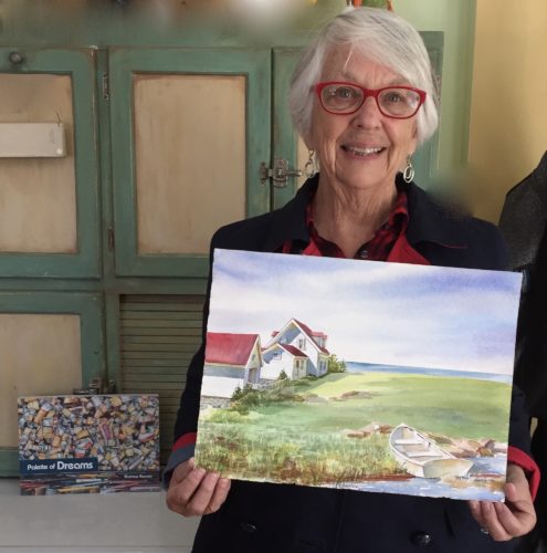 A woman holding up a watercolor painting of a house.