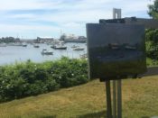 A painting on a easel in front of a harbor.