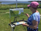 A woman painting on an easel in front of a lake.
