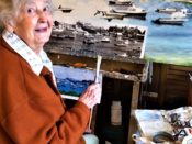 An older woman sitting in front of a painting.