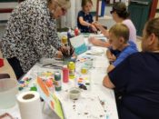 The Guild of Harwich Artists hosted a successful community art event, with a group of people sitting at a table painting.