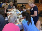 The Guild of Harwich Artists hosted a successful community art event, with a group of people sitting at a table and painting.