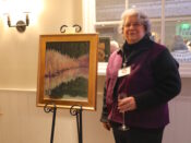 A woman standing next to a painting on an easel.