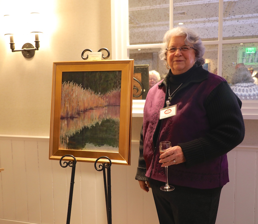A woman standing next to a painting on an easel.