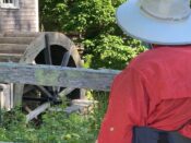 A person in a hat looking at a water wheel.