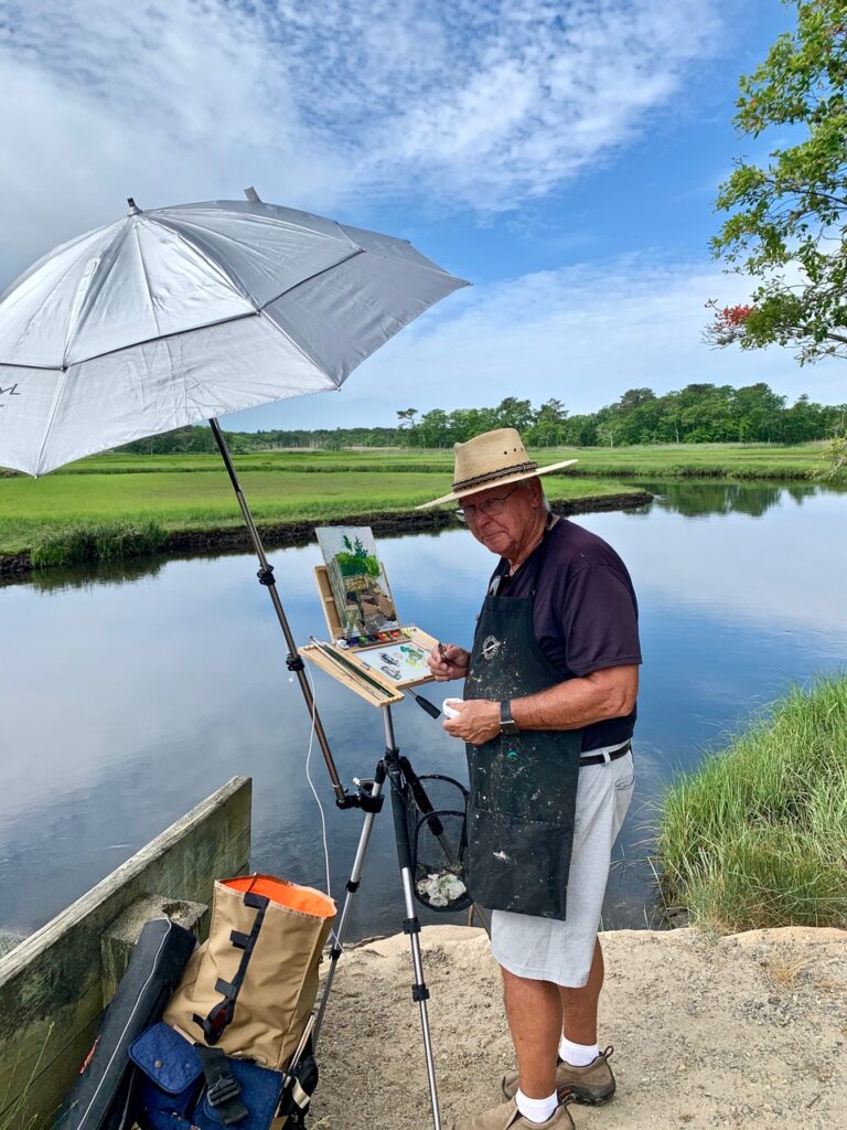 A man holding an umbrella while painting near a body of water.