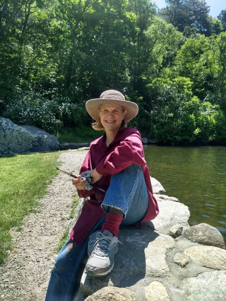 A woman in a hat sitting on a rock next to a lake.