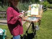 A woman holding an easel in a grassy area.
