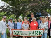 A group of people standing in front of a banner that says art in the park.