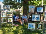 A group of people sitting in a grassy area with framed pictures.