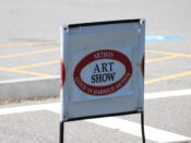 A sign for an art show in a parking lot.