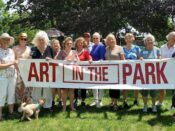 A group of people holding a banner that says art in the park.