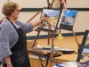 A woman in an apron is painting on an easel.