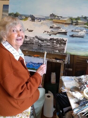 An older woman sitting in front of a painting.