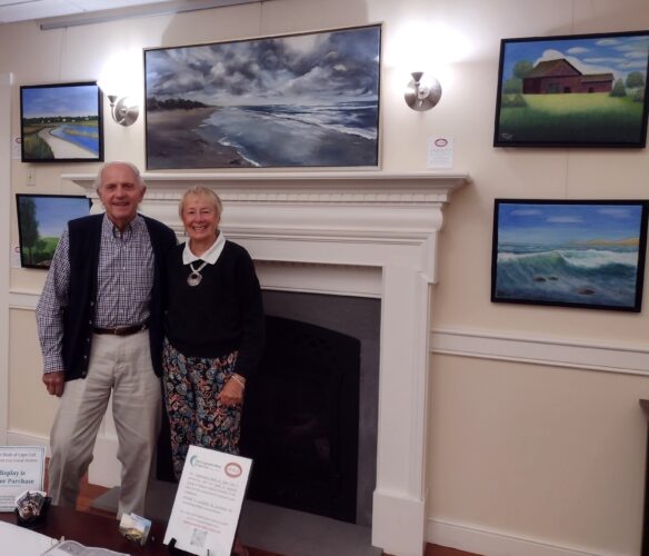 Two people standing in front of a fireplace with paintings on the wall.