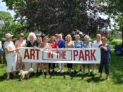 Group of people holding "Art in the Park" banner.