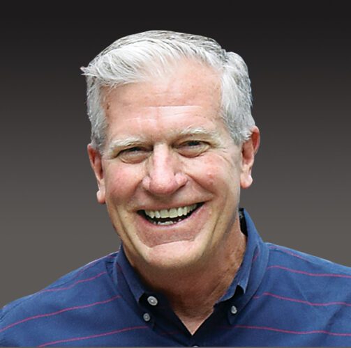 Smiling man with gray hair against dark background.